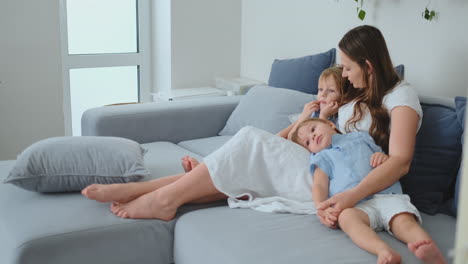 Mom-in-a-dress-and-young-children-sit-on-the-couch-and-watch-your-favorite-TV-series